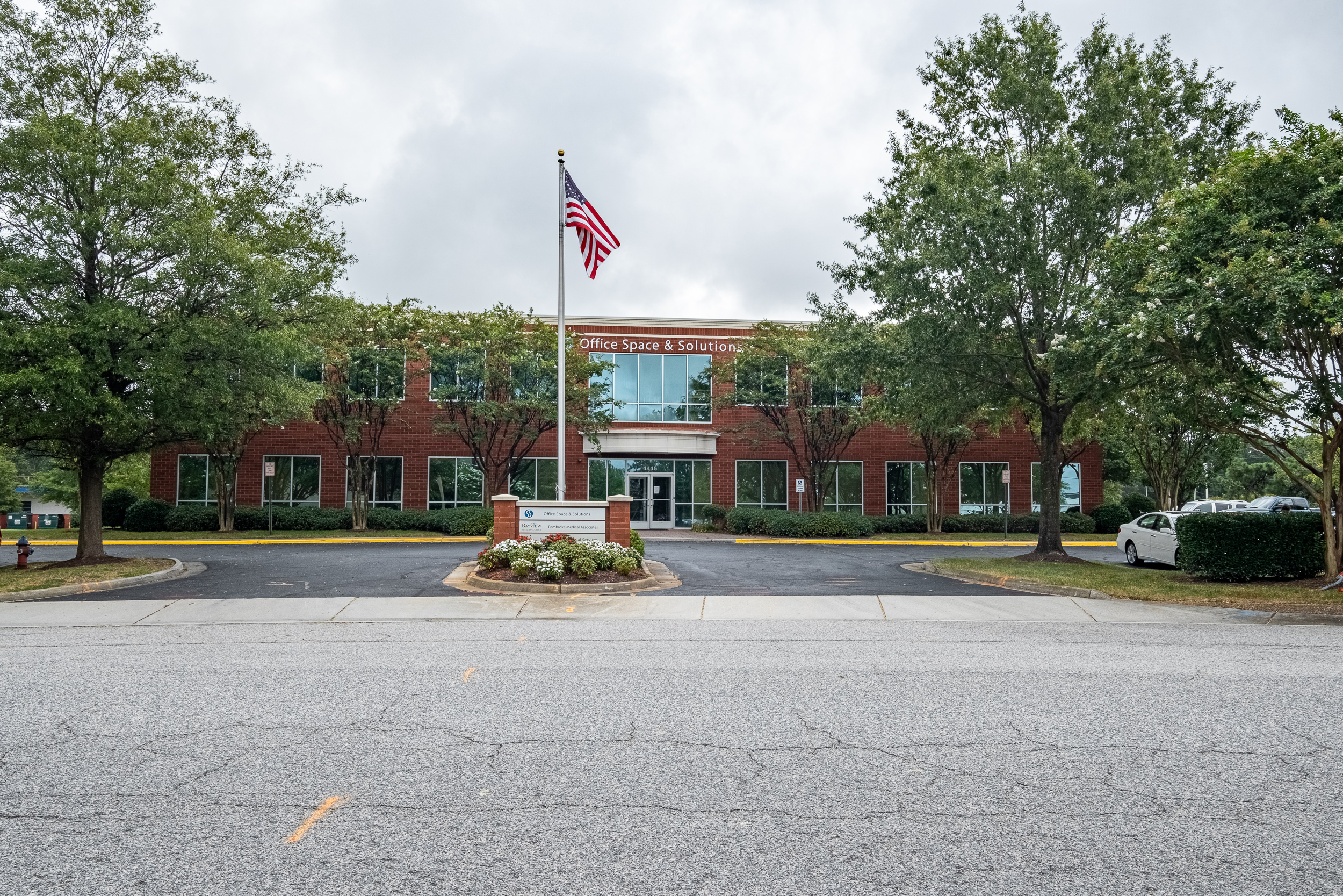 OSS Headquarters, Virginia Beach VA. Exterior of main headquarters brick building, with Office Space and Solutions signage and American flag flying on a large flag pole.